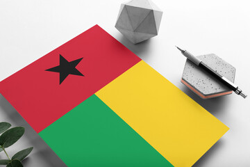 Guinea flag on minimalist paper background. National invitation letter with stylish pen on stone. Communication concept.