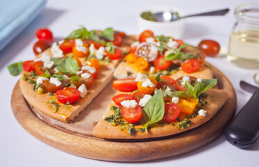 Homemade pizza with cherry tomatoes, fresh green basil and feta cheese. Homemade food. Concept for a tasty and hearty meal. Wooden background. Close up.