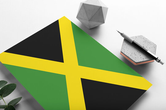 Jamaica flag on minimalist paper background. National invitation letter with stylish pen on stone. Communication concept.
