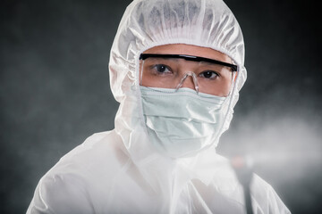 Professional cleaning staff with a To wear protective medical mask and PPE suit use chemical sprayer protect decontamination indoors. remove bacterias, viruses, and infections from the surface. COVID-