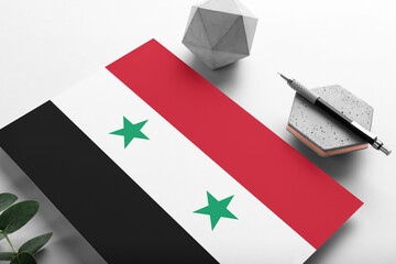 Syria flag on minimalist paper background. National invitation letter with stylish pen on stone. Communication concept.