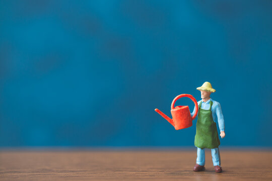 Miniature people gardener standing in front of a blue wall background
