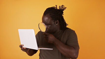 Close up shot of an african man using magnifying glass to read from laptop screen.