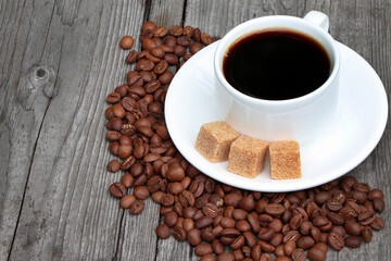 A cup of coffee with coffee beans and cane sugar on a wooden background.Heap of coffee beans. White coffee cup and saucer. Espresso coffee. Old wooden table.