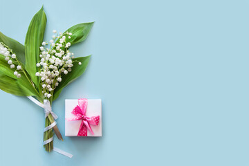 A bouquet of spring lilies of the valley and a gift box with a pink ribbon on a blue background