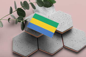 Gabon flag on hexagon stylish stones. Pink copy space background. Flat lay, top view minimal...