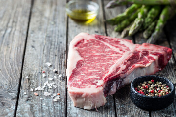 Raw T-bone Steak with fresh herbs and oil on dark wooden background