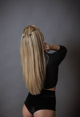 A slender girl in black underwear and long blond hair stands with her back turned