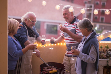 Group of happy senior friends enjoy together a barbeque night at home in outdoor terrace - mature people in friendship have fun in party bbq food activity