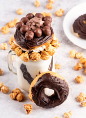 Chocolate donut milkshake decorated with caramel popcorn, whipped cream and candies