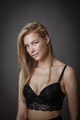 a blonde girl in a black bra poses in a Studio on a dark background
