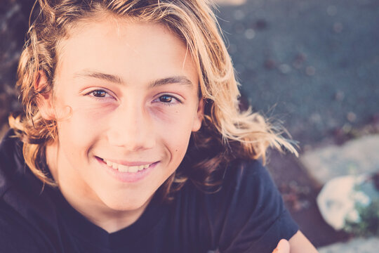 Young handsome male teenager in cheerful portrait with long blonde hair surf style - beautiful teen children looking on camera smiling and happy