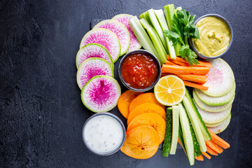 Buddha bowl of mixed raw snacks. vegetables with sauces carrots, cucumber, persimmon, celery and radishes, top view, flat lay