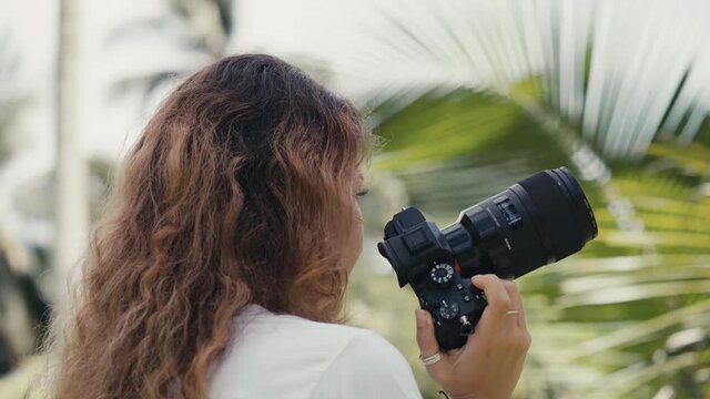 a woman photographer standing in the jungle while camera is rotating and moving around her. Close-up of full 360 degree rotation. Tracking Arc Shot