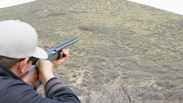 clay pigeon flies and man shots it with a shotgun in slow motion.