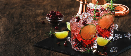 Fototapeta na wymiar Red alcohol cocktail with cranberries, ice and rosemary on wooden background, copy space