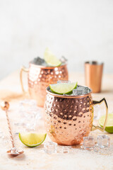Cold Moscow Mules cocktail with ginger beer, vodka, lime. White stone background.