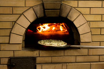 Pizza roasting in the oven with wood burning fire in the oven. Wooden firewood is burning in the...