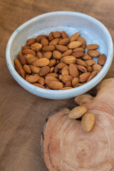 Two almonds in a shell on a wooden surface. Ceramic pale blue plate with peeled almonds on a pale brown canvas. Copy space. Vertical image. Selective focus.