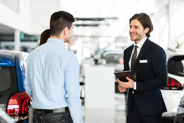 Salesman Offering Couple Car Standing In Auto Showroom