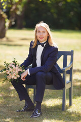 Young man weared in classic suit outdoors in his wedding day. Blonde man with long hairs. Young man or groom in a garden. Groom preparing to wedding