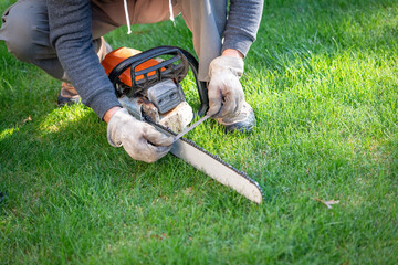 Man uses a file to sharpen an orange chainsaw in the green grass