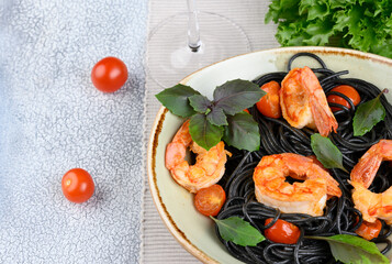Black plate with black Nero spaghetti with langoustines, cherry and garlic, green lettuce leaves and cherry tomatoes