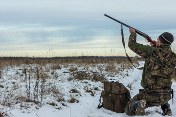 Hunting for wild animals. Hunter with a gun on the field on a cloudy sky background