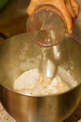 Female hand pouring water into a dish with flour.