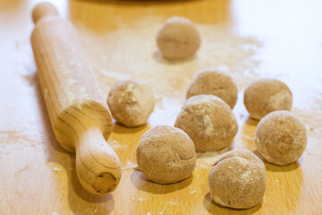 High angle view of balls of integral dough and wooden rolling pin on a kitchen table.