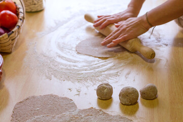 Close up of female hands using a wooden rolling pin on a kitchen table.