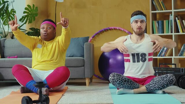 Oversize and slim retro guys team practicing yoga and meditation, sitting on mats together training workout at home. Fake fitness. Concept of sports, fun, joke.