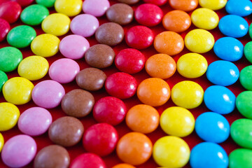 Rainbow pattern of round colored chocolates. Sweets shot closeup on red background. Selective focus