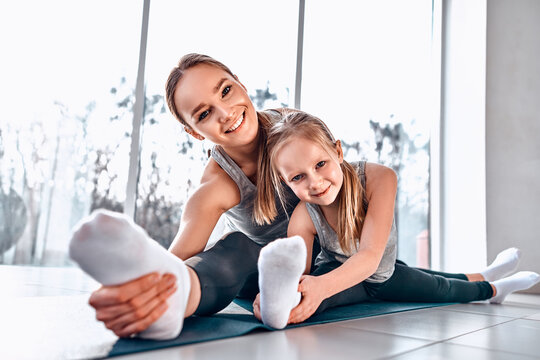 Mom and daughter do exercises on the mat. Mom with a child on a yoga mat smiling and sitting on the splits. Health family doing pilates.