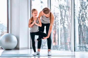 portrait of mother gently teaching her small girl his first yoga notions careful near kids body helping daughter finished action in the fitness class at school.