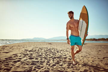 Naklejka na ściany i meble Handsome man with a surf board on the beach.