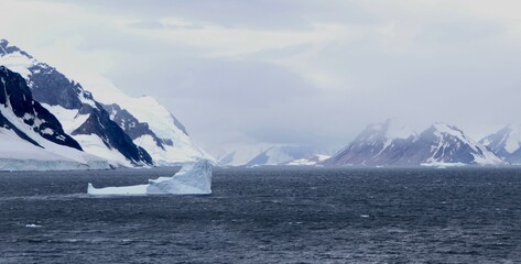 Iceberg before glacier landscape and dark, snowy mountain, Antarctica