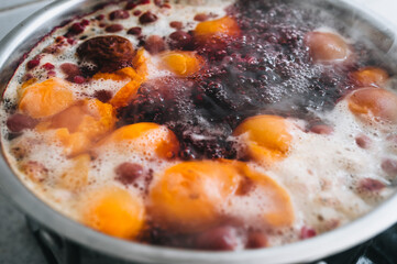 Fresh fruits are boiled in boiling water in a metal pan on a stove with bubbles and foam close-up. Cooking a delicious compote of apricot, apples, cherries, raspberries. Photography, concept.