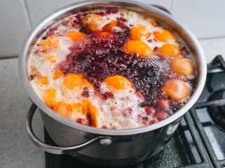Cooking a delicious compote of apricot, apples, cherries, raspberries. Fresh fruits are boiled in boiling water in a metal pan on the stove. Photography, concept.