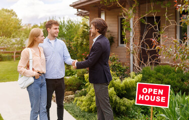 New home owners shaking hands with real estate agent near residential building outside, copy space