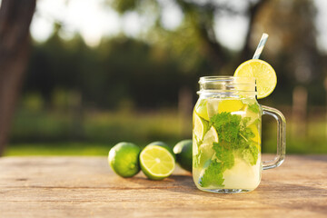 Homemade lemonade mojito in mason jar on wooden table. Lime slices and mint leaves. Fresh drink outdoors in the garden.