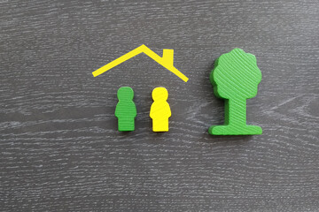 Two figures of people under the roof of a house, a tree on a dark background. Family, real estate. Housing market.