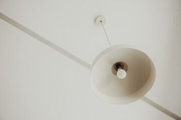 White industrial and minimalist lamp hanging on a white roof. Minimalist concept. Minimalist stock photos. Aesthetic composition.
