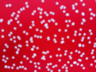Scattered white snowflakes on red background. Simple festive flat lay. Stock photo.
