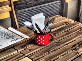 Budapest, Hungary - June 12, 2020: Red polka dot mug with cutlery and a menu card on a wooden table on a restaurant terrace in the city centre in dramatic tone