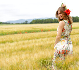 Slim pretty girl in rye field staying in yellow dress with poppy flowers in hand