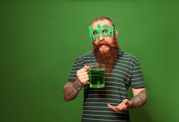 Bearded man in party glasses with green beer on color background, space for text. St. Patrick's Day...