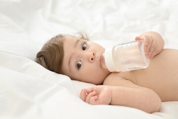 Cute little baby with bottle on bed