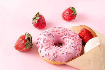 donut with pink icing, fresh strawberries in an envelope on a pink