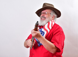 Happy, smiling old man, armed with a sawed off rifle, wearing patriotic colors, eyeglasses and a floppy western hat. - obrazy, fototapety, plakaty